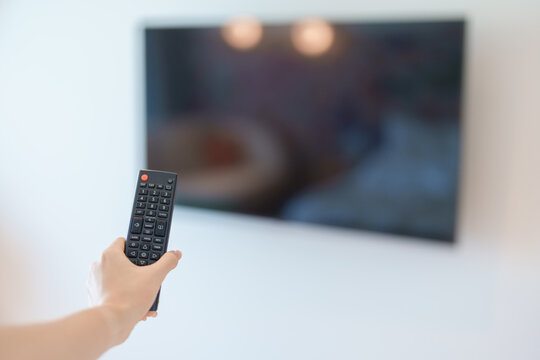 hand using remote controller press button for adjust Smart TV in modern room at home. Woman holding remote control,  switch channel, searching new interesting program, Turn on or off on Television