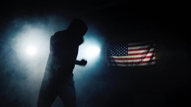 A male boxer shadowboxing with intensity in a dark, smoky gym with american flag in background, dynamic footage.