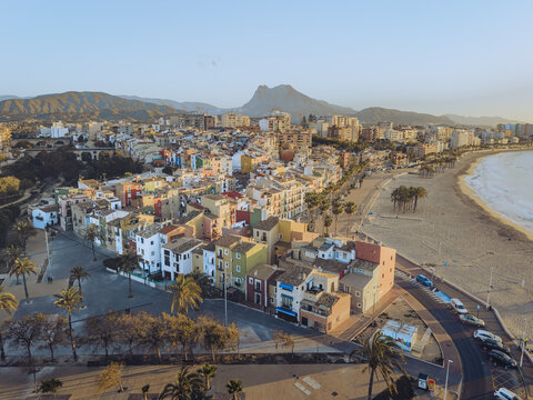 Aerial view of the colorful houses along the coastline with a sandy beach and mountains under a clear sky in La Vila Joiosa, Valencian Community, Spain.