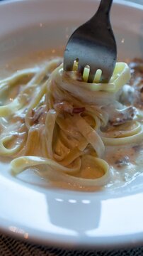 Twirling Creamy Fettuccine Carbonara Pasta with a Fork in White Bowl