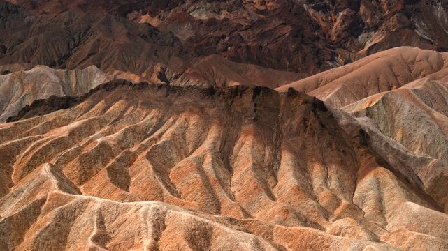 Stunning aerial view of Zabriskie Point's eroded badlands in Death Valley National Park featuring deeply carved mudstone ridges bathed in warm golden hour light with intricate textures and layered.