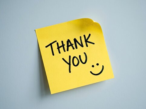 Yellow sticky note with handwritten "Thank You" message and a smiley face, on a cool grey backdrop, gratitude Concept