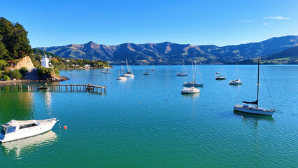 Obraz premium Aerial view of sailboats in Akaroa Harbor with lighthouse and mountains