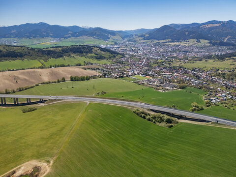 Aerial view of the D1 motorway viaduct crossing vibrant green fields with the town and rolling mountains under a clear blue sky Likavka, Zilina Region, Slovakia.