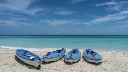Obraz premium Row of canoes with paddles on a sandy beach. The waves of the endless turquoise ocean are foaming on the sand. Blue sky, clouds. Cuba. Varadero. Resort.