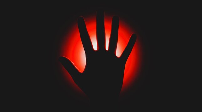 Silhouette of a human hand raised against a glowing red circular light source in the dark