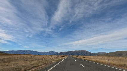 Naklejka premium Long Straight Road Through Autumn Landscape Toward Distant New Zealand Mountains