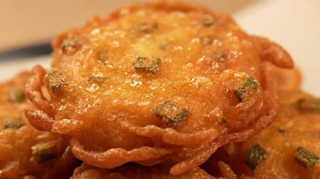 Extreme close-up of a crispy, deep-fried fritter (pakora or bhaji) showcasing the golden brown texture and herbaceous flecks, ideal for appetizing street food or snack concepts.