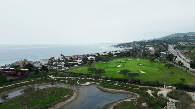 A golf course bordered by coastal homes and the ocean under overcast skies. Suitable for real estate or travel content.