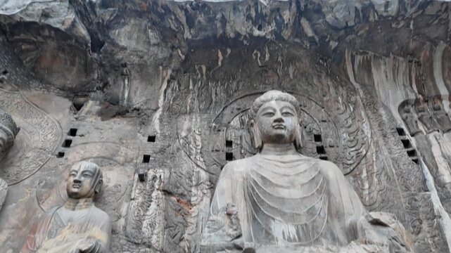 Majestic stone Buddha reliefs carved into Longmen cliff face, featuring intricate halos, attendants, and weathered ancient artistry