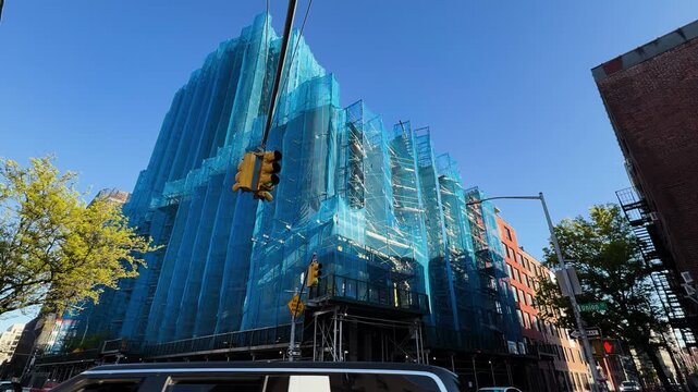 Traffic passes construction site with building under blue mesh safety netting on sunny day