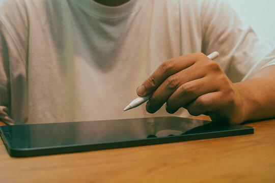 Person using stylus pen on digital tablet on wooden desk for creative work and note taking