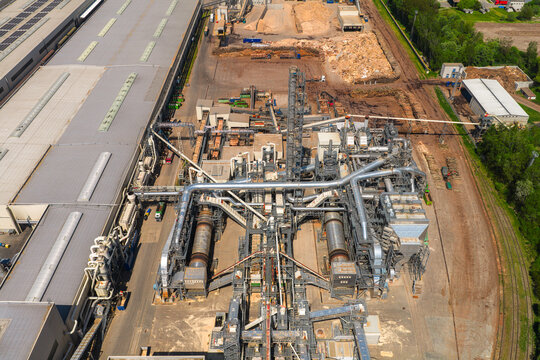 Aerial view of an industrial wood processing facility with complex piping systems, storage yards for wood chips, and large factory buildings in Jihlava, Vysocina Region, Czechia.