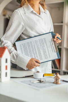 Professional female realtor holding contract documents in office. Real estate consulting, property sales and rental agreement concept with client service and modern housing solutions.