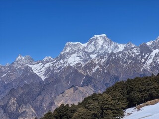 Obraz premium Majestic Hathi Ghodi peak towering above pine forests and snow patches near Auli, Uttarakhand.