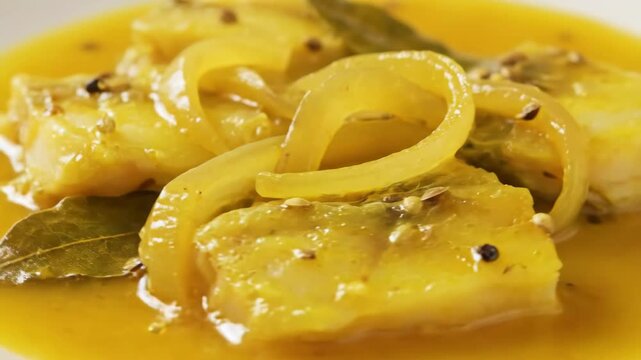 Delicious close-up of tender white fish chunks, such as cod or pollock, simmered in a vibrant yellow sauce with sliced vegetables, bay leaves, and aromatic spices.