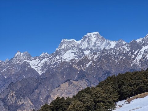 Majestic Hathi Ghodi peak towering above pine forests and snow patches near Auli, Uttarakhand.