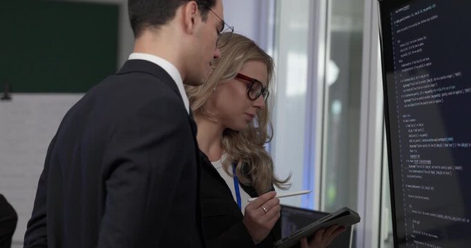 Two professionals analyze and discuss programming code displayed on screen in modern tech workspace. Capturing a collaborative environment focused on software development, debugging, and teamwork
