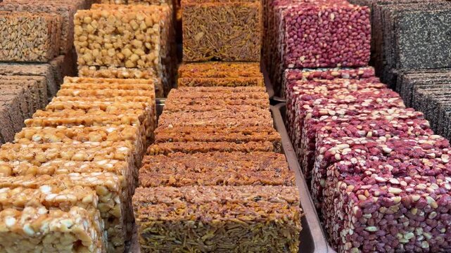 Rows of neatly arranged traditional Chinese peanut, sesame, and sunflower seed brittle cakes at a food stall showing rich textures and ingredients.