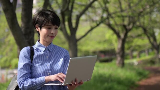 新緑を背景にノートパソコンを見るビジネスウーマンのズームインショット