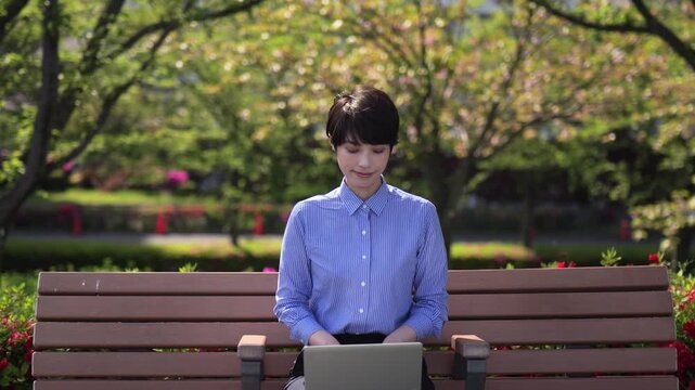 新緑を背景にベンチに座ってノートパソコンを見るビジネスウーマンのズームインショット