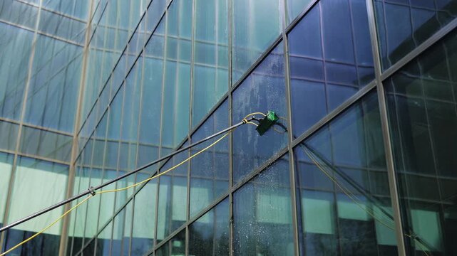 Automated system cleans a high-rise glass facade with precision and efficiency. Water sprays and brushes move, leaving surfaces pristine. Modern technology cleaning, automated robotic window cleaner