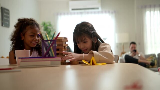Two young school children are happily playing a game of Jenga, supervised nearby by their teacher