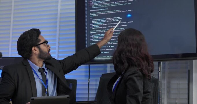 Two professionals analyze and discuss programming code displayed on screen in modern tech workspace. Capturing a collaborative environment focused on software development, debugging, and teamwork
