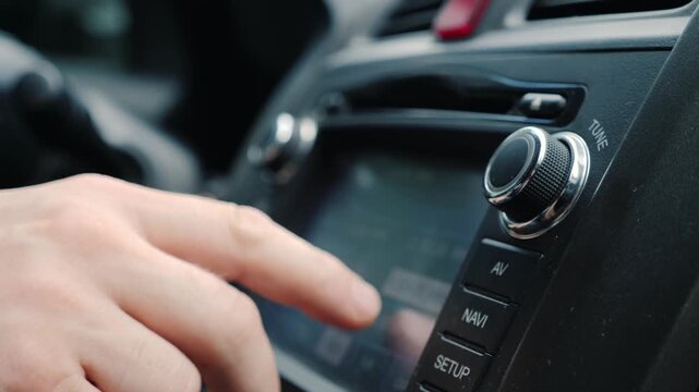 Male hand adjusting car multimedia system and rotating tune knob on dashboard while driving on road.