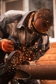 Industrial worker in protective gear cutting large metal pipe with angle grinder in workshop. Flying sparks and powerful tools create dynamic scene of heavy industry and skilled craftsmanship.