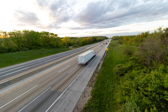 A slow shutter photo creating blur of a white semi truck with a white trailer driving down the highway road. 