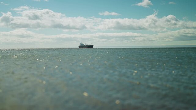 Wide shot of a massive merchant ship navigating the calm waters of the Magellan Strait on a sunny day.