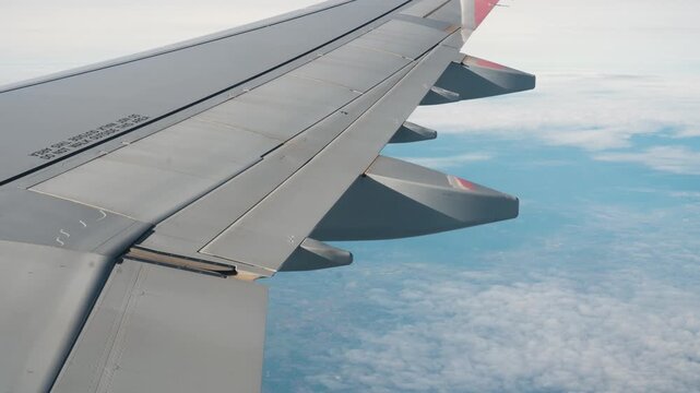Passenger airplane wing flying over thick white clouds under blue sky, aerial view