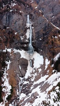 Vertical, aerial: establishing drone shot of Engstligen Falls with snow during the day, second highest fall in Switzerland