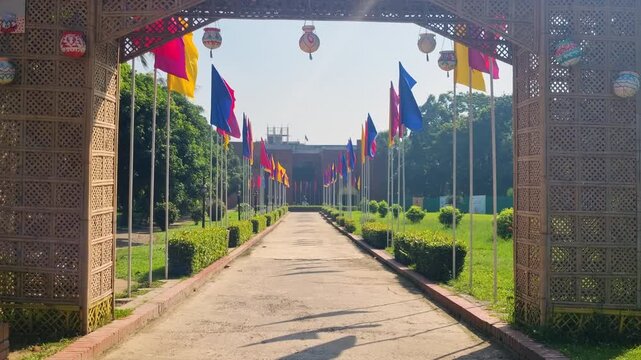 Entrance gate and pathway leading to the Shilpacharya Zainul Folk and Craft Museum in Sonargaon, Bangladesh with colorful flags swaying in the wind on a clear sunny day at this cultural landmark