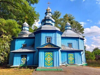 Historic St. Pokrova wooden church in Horbuliv village, Ukraine. A beautiful example of traditional blue-painted Ukrainian folk architecture with golden domes against a bright blue summer sky.  © Vasyl