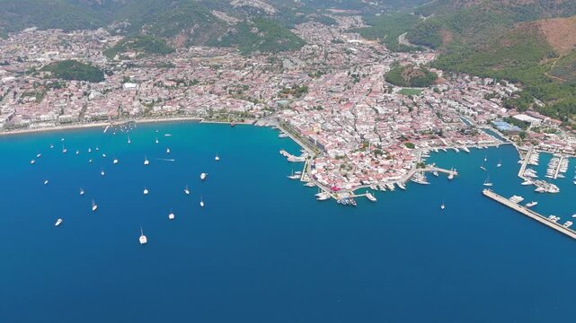 Marmaris, Turkey. Sweeping aerial panorama of the natural harbor and yacht-filled bay, backed by pine-clad mountains and the terracotta rooftops of the coastal resort under clear summer skies. Aerial