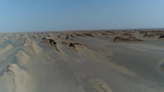 Aerial perspective shows wind-sculpted yardang rock with sharp edges and surrounding sand dunes under intense sunlight in Iranian desert cinematic stock footage.