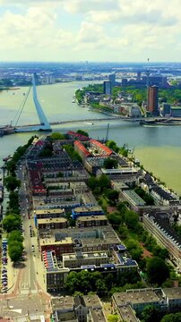 Vertical video. Rotterdam, Netherlands. Erasmus Bridge, its 139-metre steel pylon and 40 stay cables spanning the Nieuwe Maas, Drone footage over Noordereiland with the city skyline beyond. Drone foo