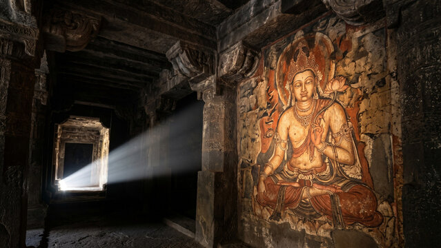 Ancient Ajanta cave Buddhist mural of serene Bodhisattva illuminated by dramatic single shaft of natural sunlight in dark cave interior with rock-cut pillars in surrounding shadow