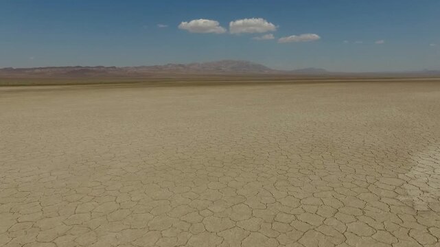 Solitary small rock sits amid expansive cracked salt crust stretching to infinity with heat haze shimmering on the horizon in Qom salt lake Iran cinematic drone video.