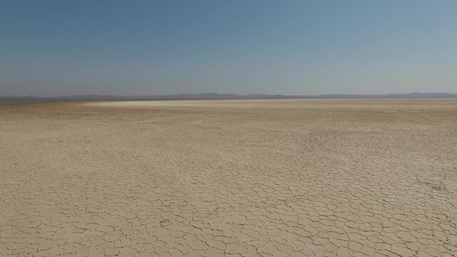 Drone captures vast empty salt flat with perfect hexagonal crack patterns and distant mountain silhouette under intense sunlight in Iranian arid region cinematic footage.