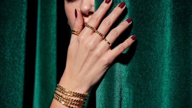 Elegant woman's hand adorned with gold jewelry against a rich emerald velvet backdrop. Close-up of a woman's hand showcasing multiple gold rings and bracelets