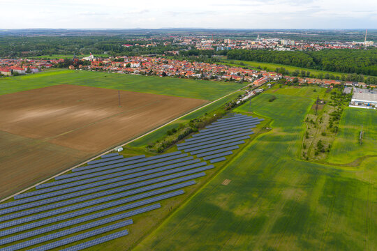 Aerial view of a solar farm with rows of photovoltaic panels in a green field near agricultural land and the town of Breclav, South Moravian Region, Czechia.
