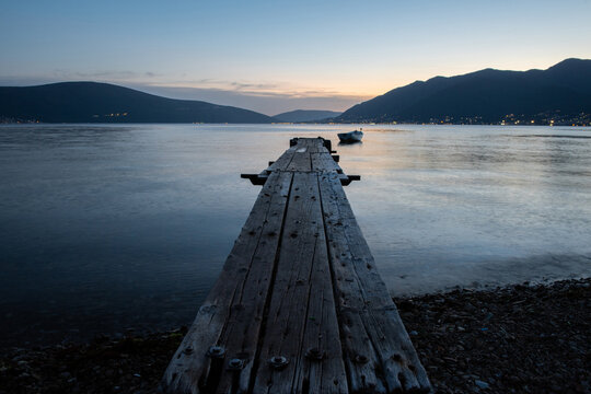 Calm wooden pier stretching into the tranquil sea at twilight, surrounded by dark mountain silhouettes and soft evening. Relaxation, meditation, philosophy, solitude, and harmony with nature. 
