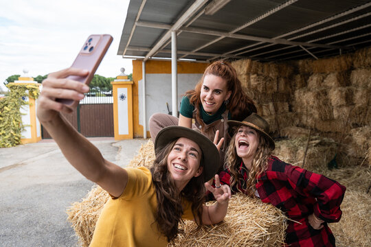 Friends taking a smartphone selfie on hay bales at a farm