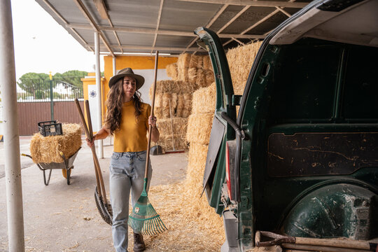 Farm worker carrying rake beside van near hay bales