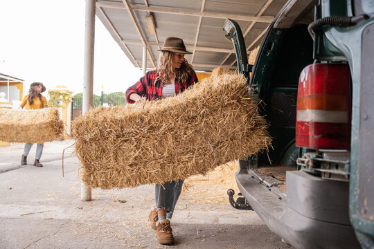 Farmer loading hay bale into van at barn