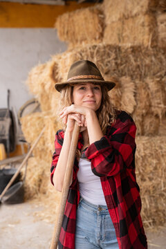 Young female farmer resting on tool in hay barn