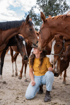 Young woman kneeling among horses at rural stable